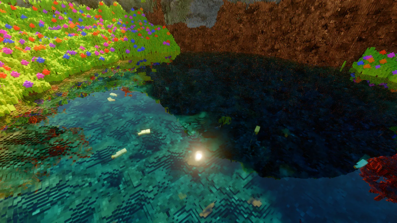 Looking down into the clear teal pond from its grassy edge, with pale fish swimming and the sun reflected on the water.