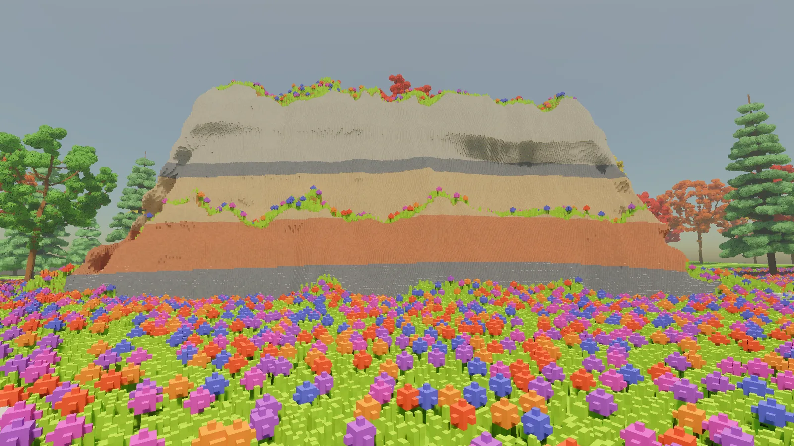 A voxel cliff rising out of the flower meadow, banded in grey, buff, red and white layers of rock, with flowers on its ledges and trees on either side.